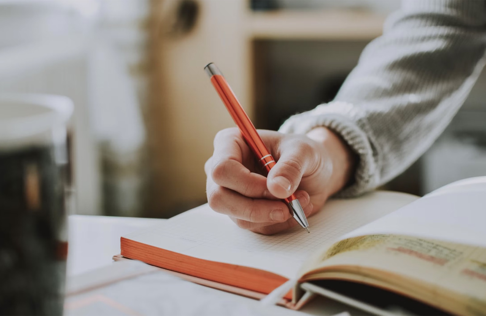 A person writing notes in a notebook beside a coffee mug while reflecting.