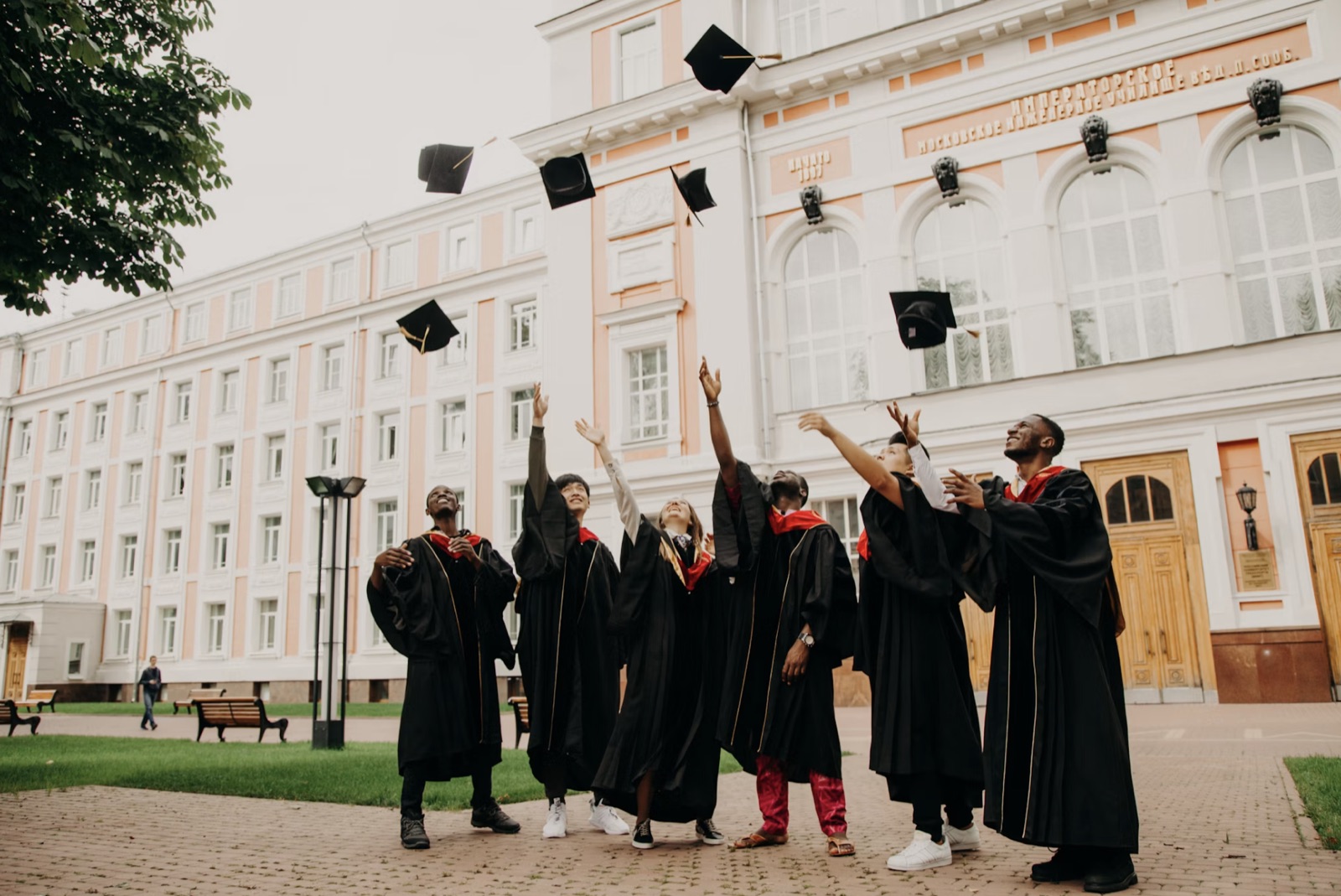 Graduates in gowns tossing their caps in front of a university building.