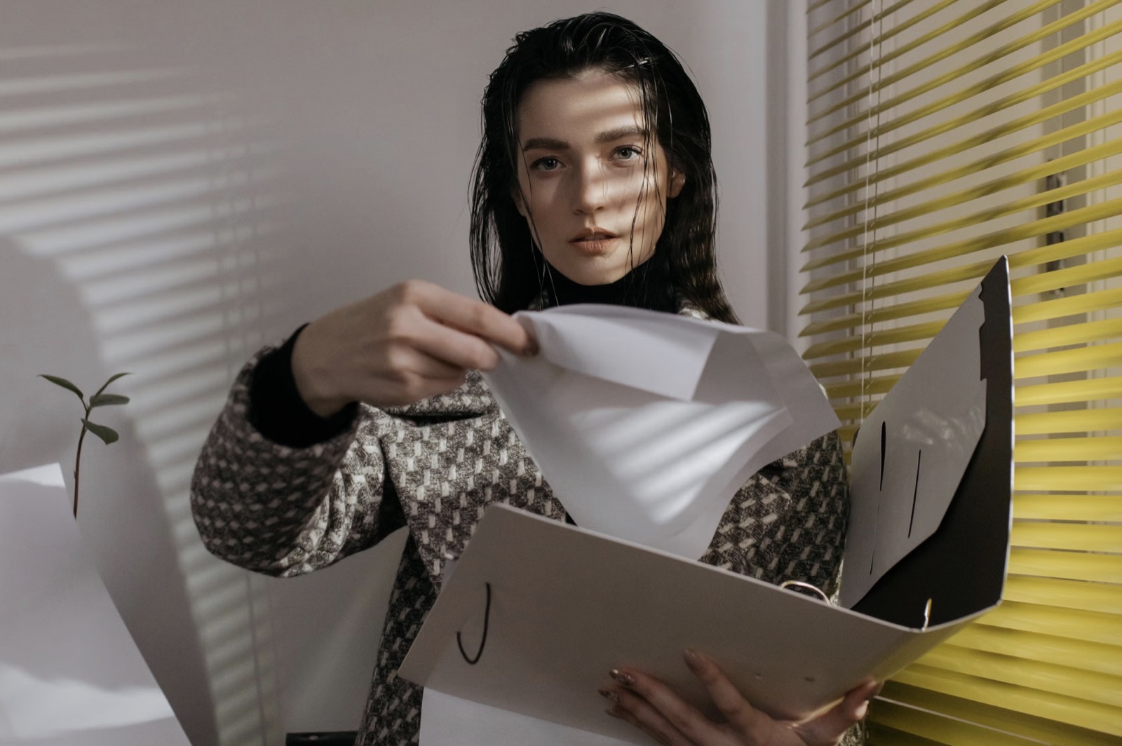A woman standing by a window sorting through papers in natural light.