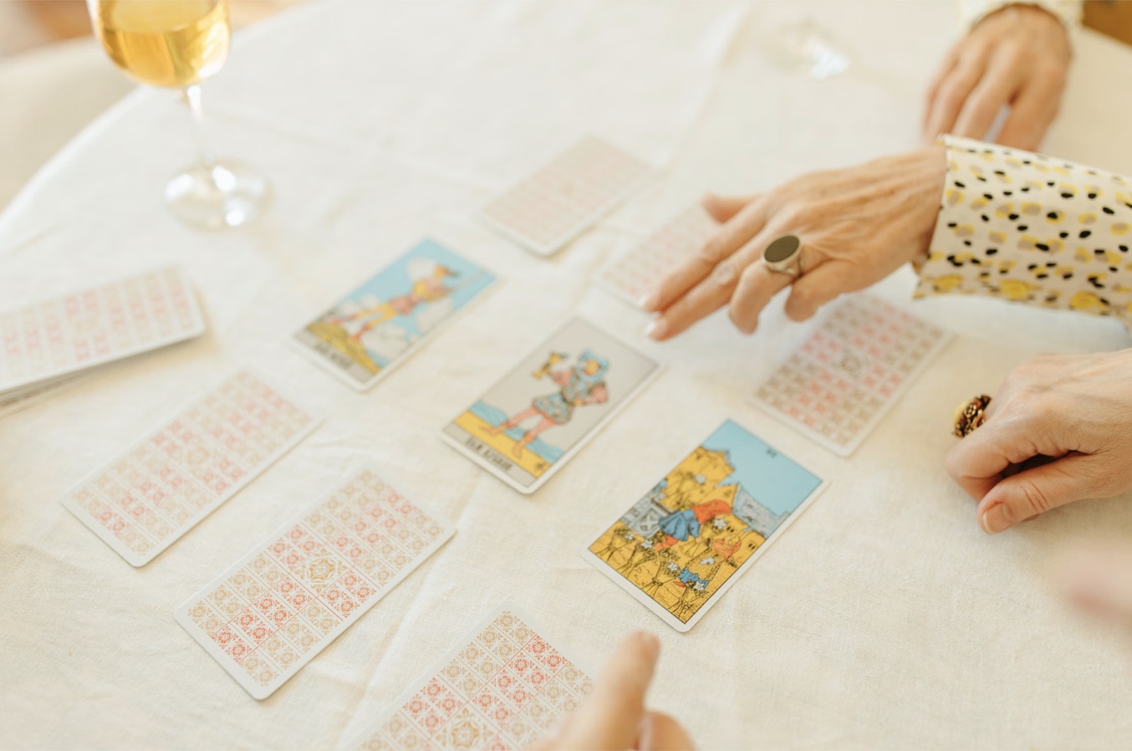Several hands gathered around a tarot spread on a white tablecloth.