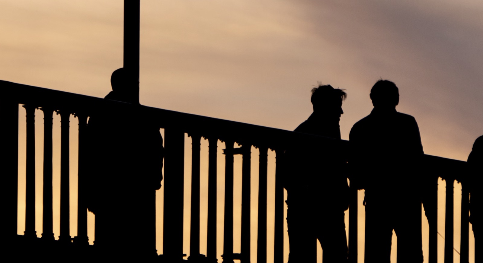 Silhouettes of two people standing on a bridge at sunset.