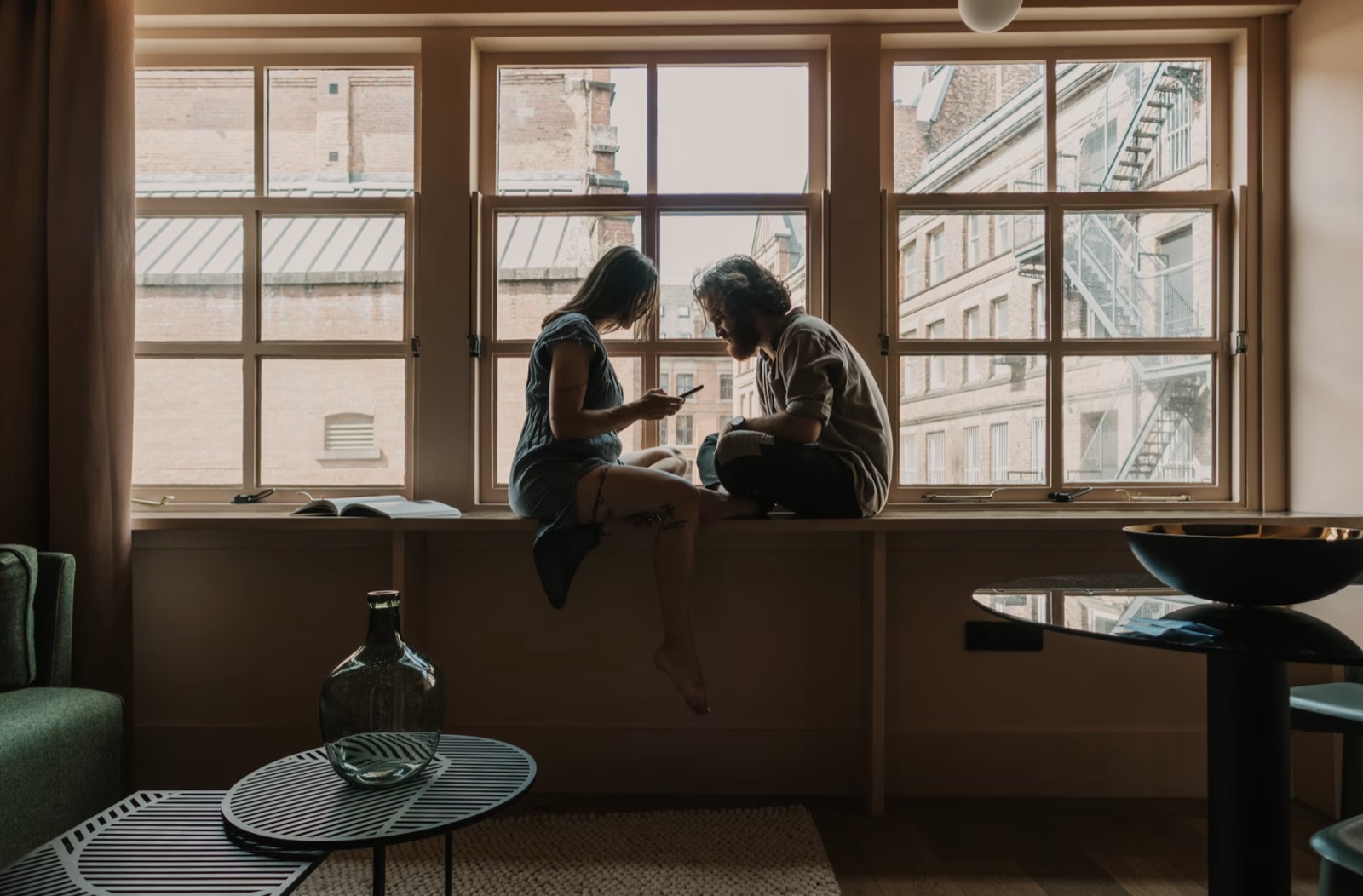 A couple sitting by a large window in quiet conversation, reflecting the emotional complexity of relationship readings.