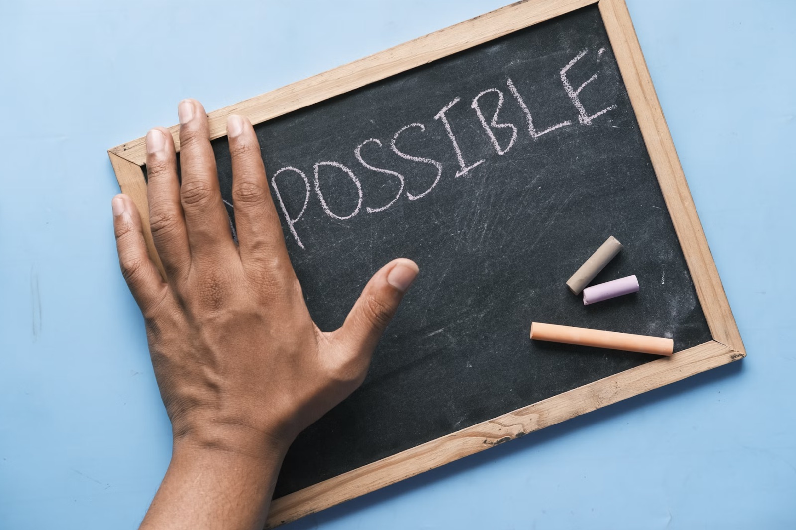 A hand resting on a chalkboard with the word POSSIBLE written across it, representing hope and forward movement.