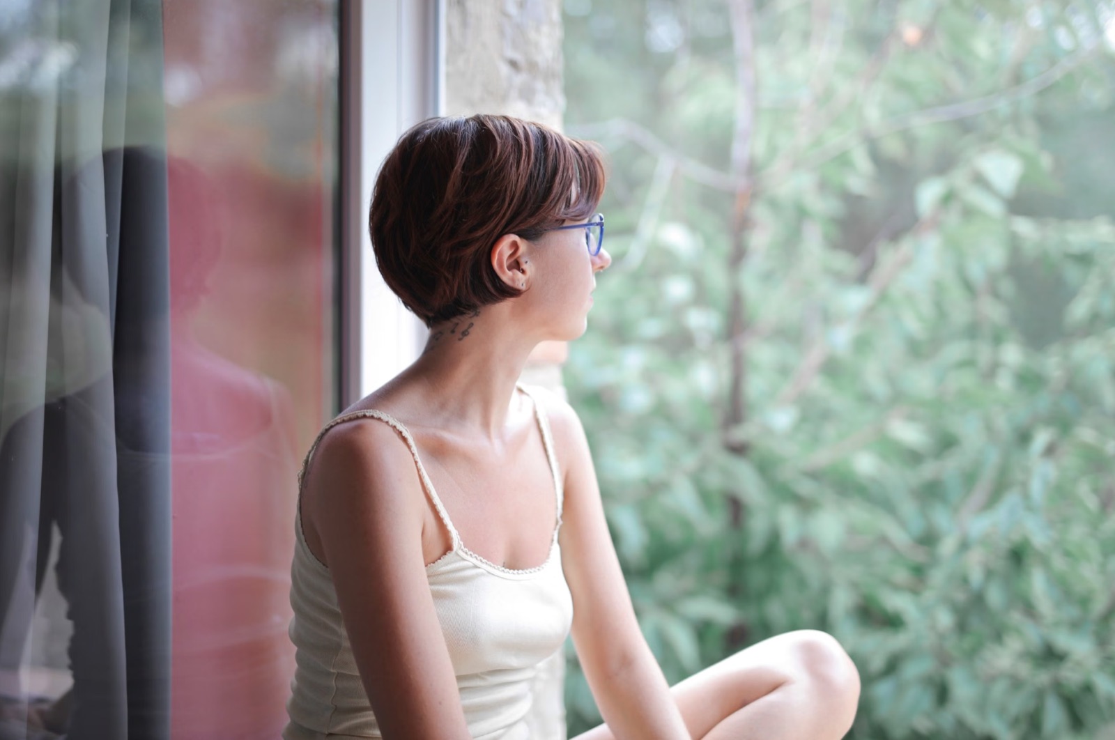 A reflective person near a window, expressing distance, disappointment, and quiet emotional strain.