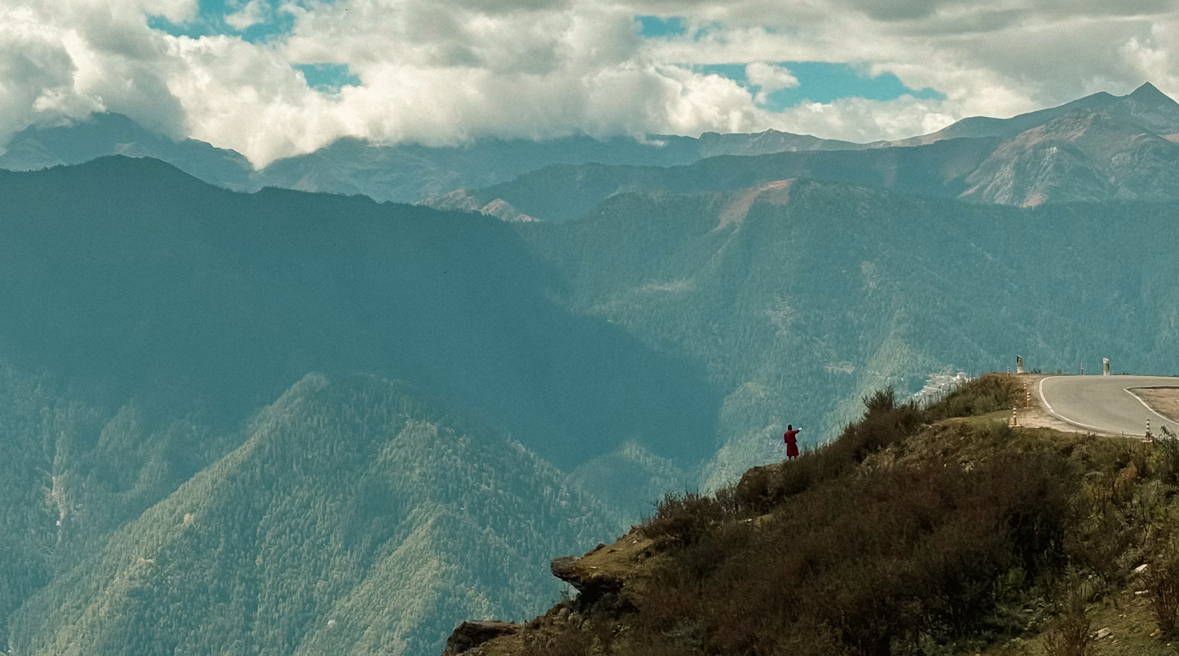 A lone figure standing high above a mountain landscape, pausing before a wider view.