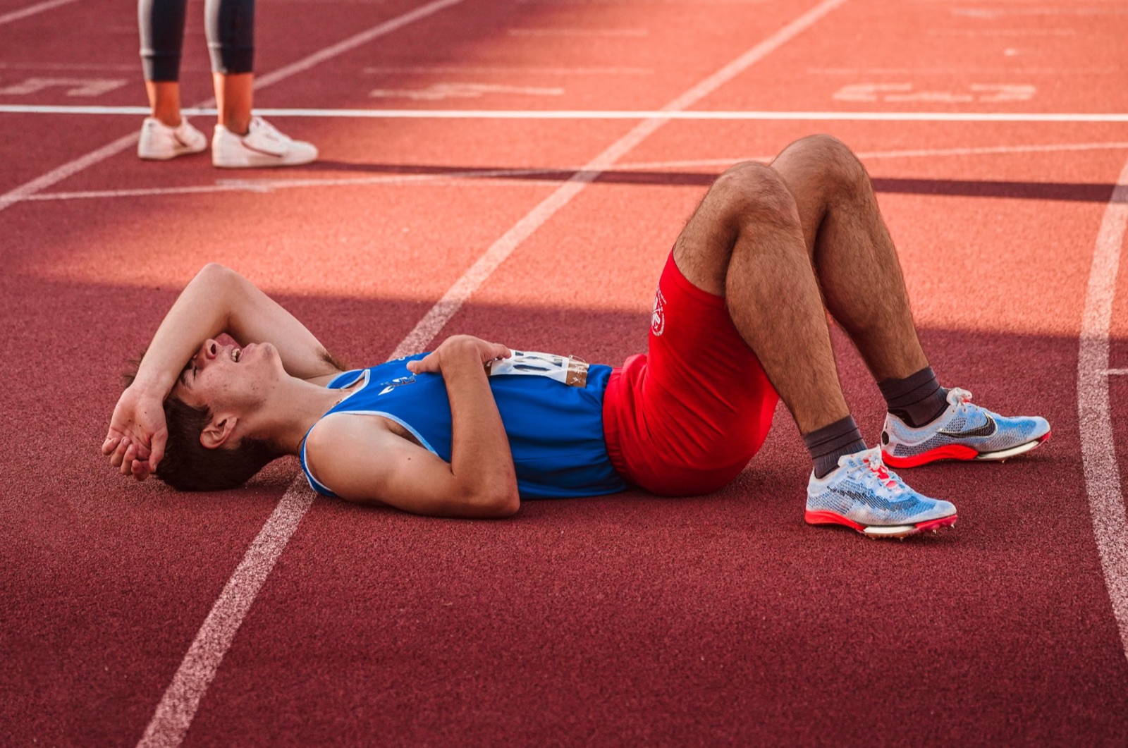 A tired athlete resting on a track after training, representing burnout, overexertion, and the shadow side of discipline.