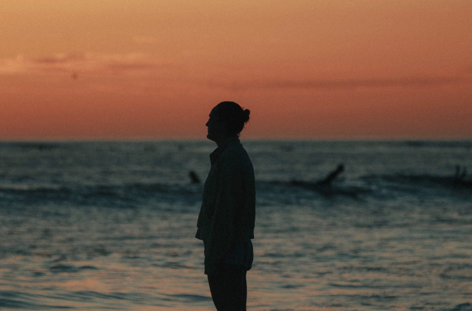 A solitary figure standing near the water at night, reflecting the isolation and emotional distance of the reversed Three of Cups.