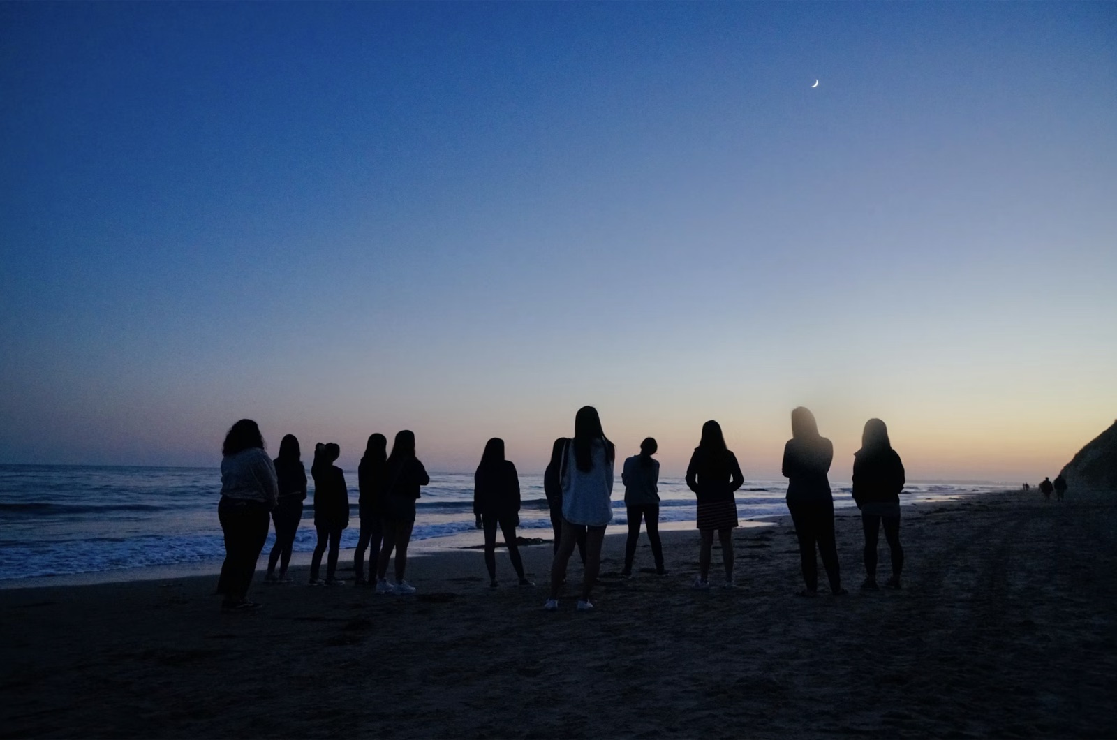 A moonlit coastal scene with women looking toward the ocean, echoing the water-sign and emotional symbolism of the Three of Cups.