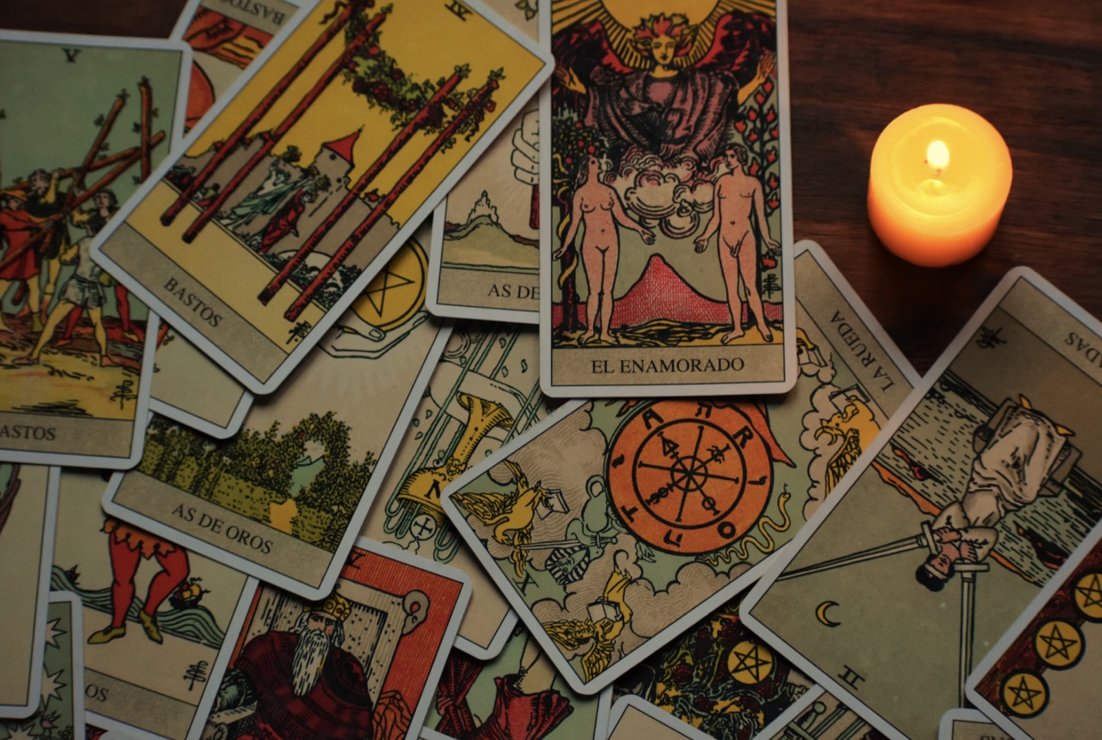 A hand holding tarot cards beside candlelight, grounding the article in a real reading atmosphere.