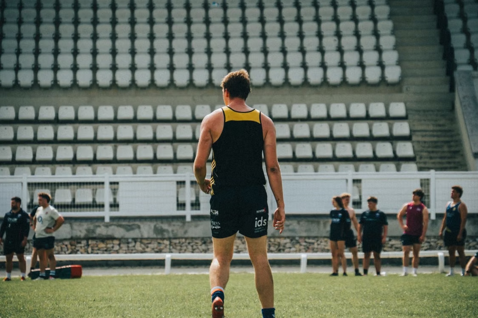 An athlete standing alone on a field while others gather in the distance, capturing effort, exposure, and the feeling of not receiving the recognition expected.