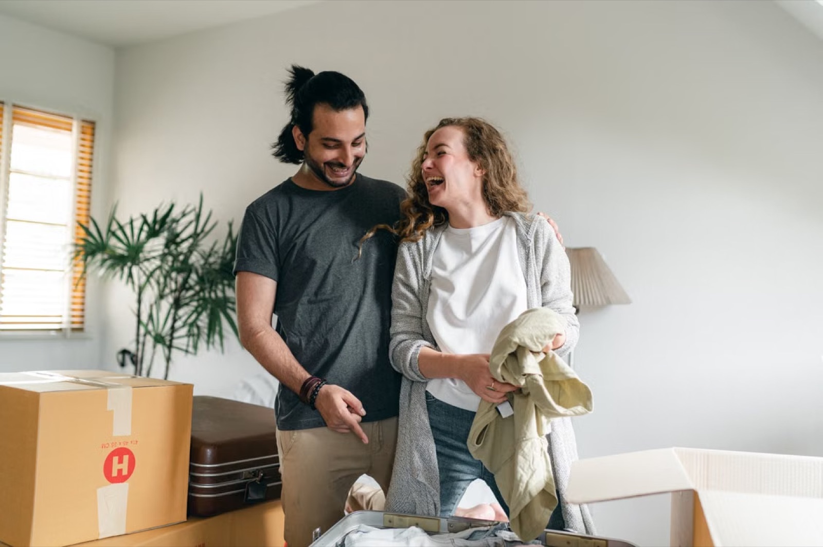 A couple happily unpacking boxes in a new home, representing commitment, homecoming, and building a shared life.