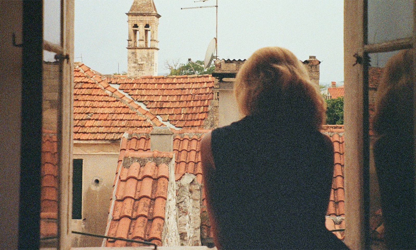 A person quietly looking out of a window, reflecting on memories and the present.