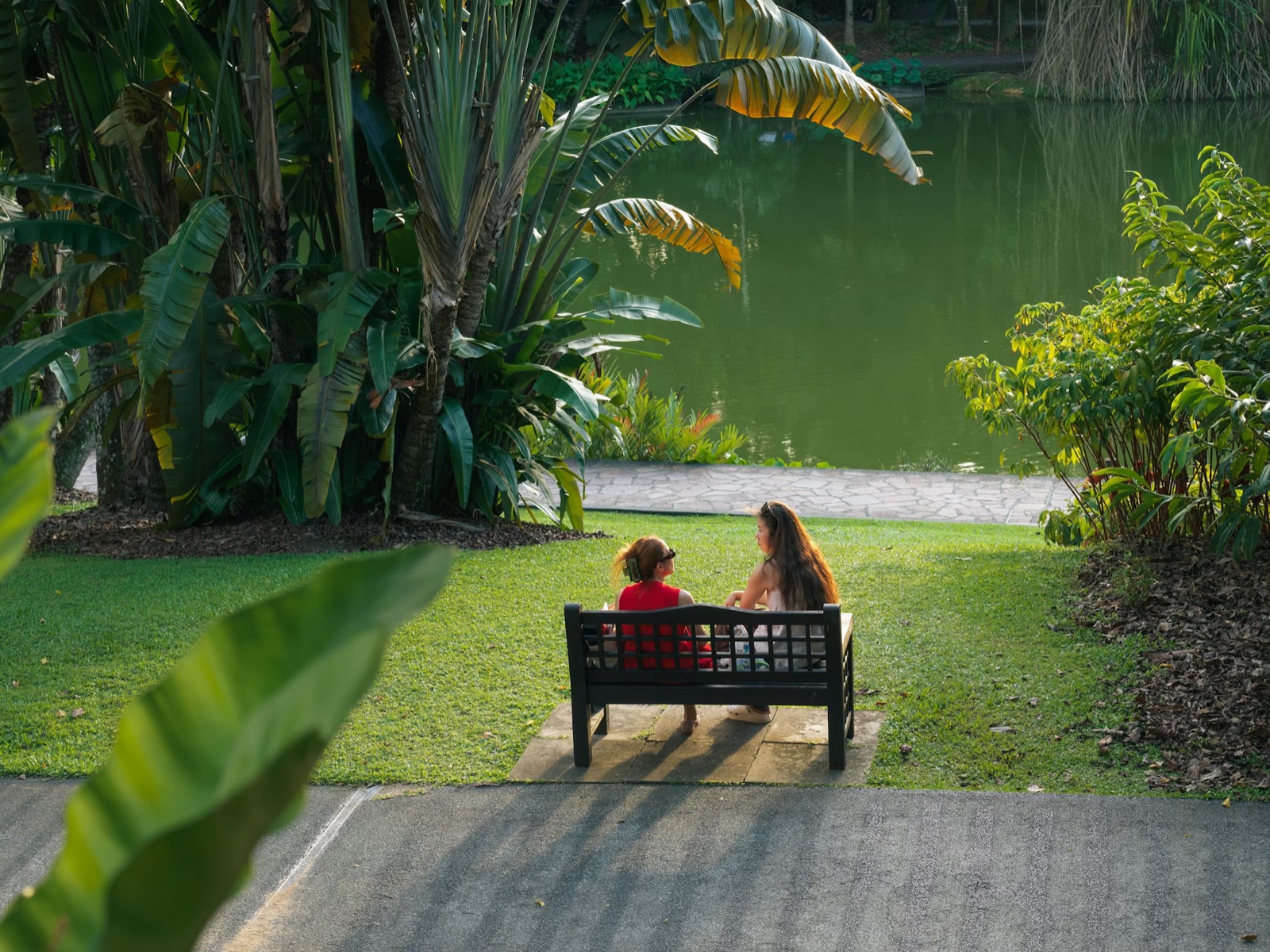 Two people sitting on a bench by the water with visible emotional distance, reflecting unresolved relationship tension.
