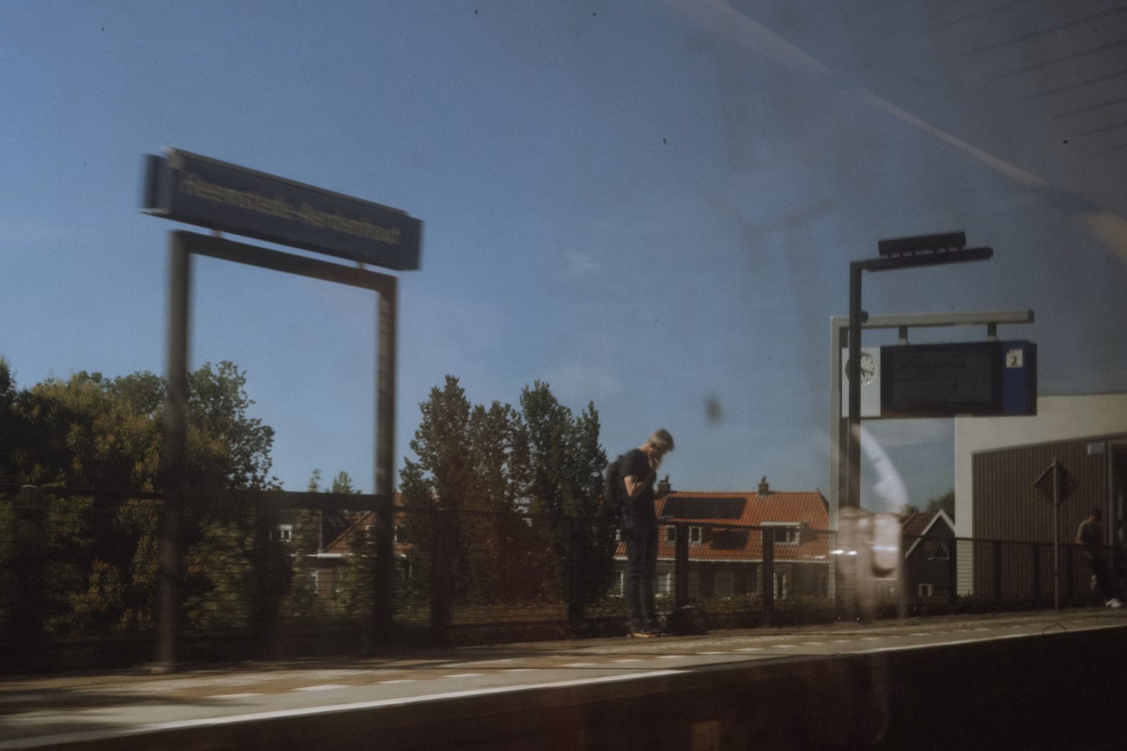 A lone traveler waiting on a train platform with luggage, representing a delayed but necessary career transition.