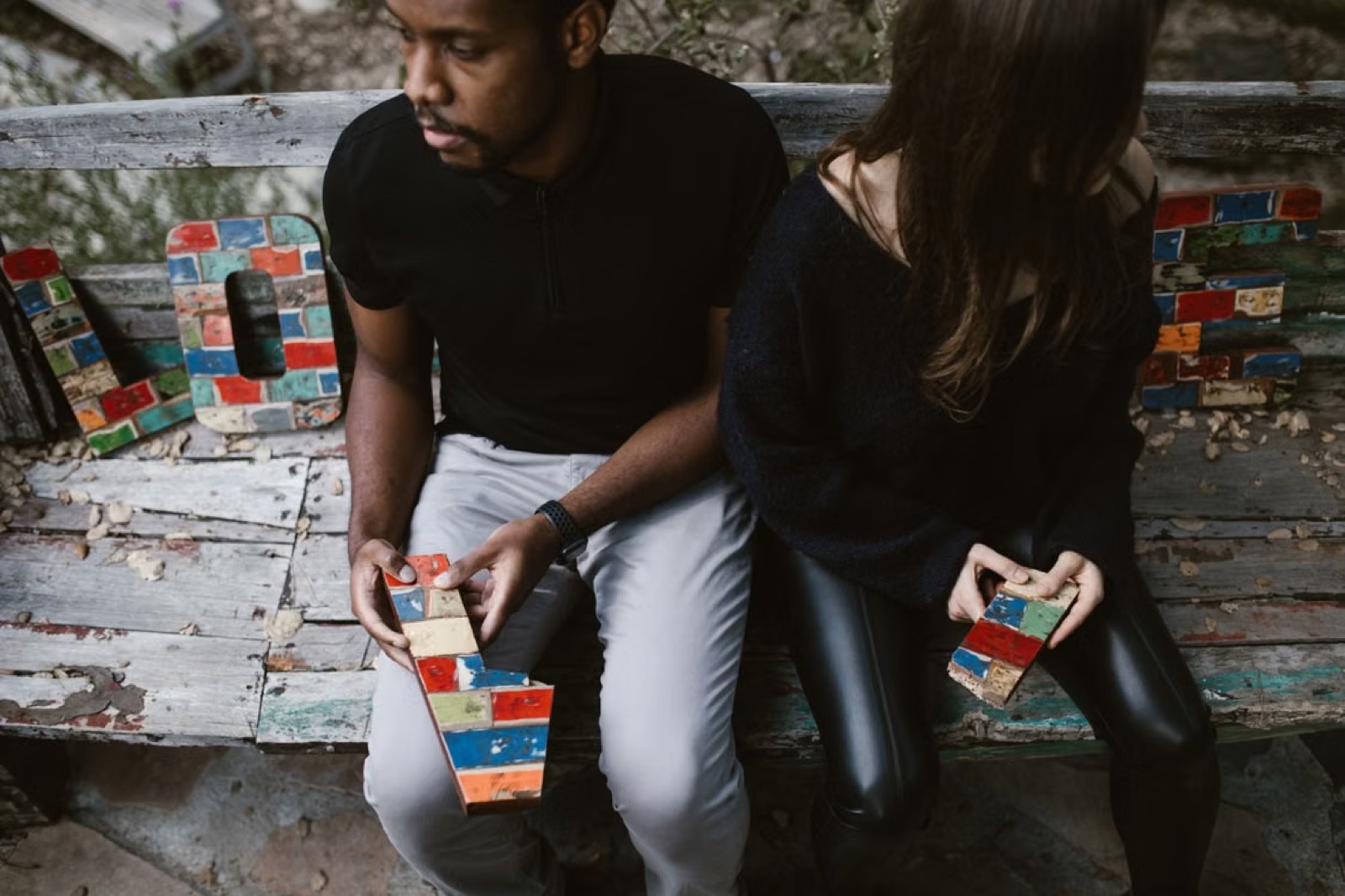 A couple sitting apart outdoors after tension, suggesting guarded love, distance, and unresolved trust.