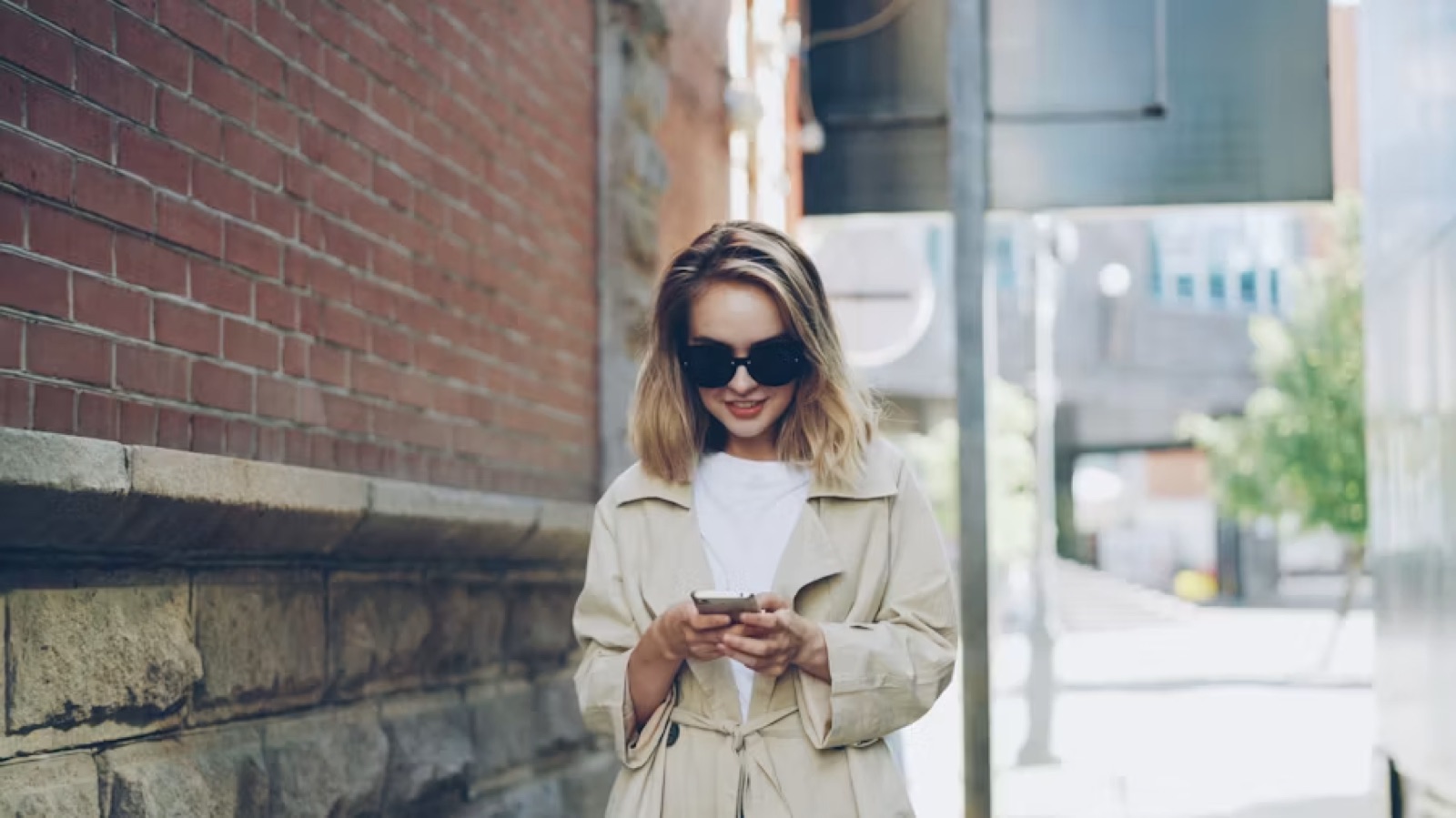 A woman outdoors smiling at her phone, open to a real new connection.