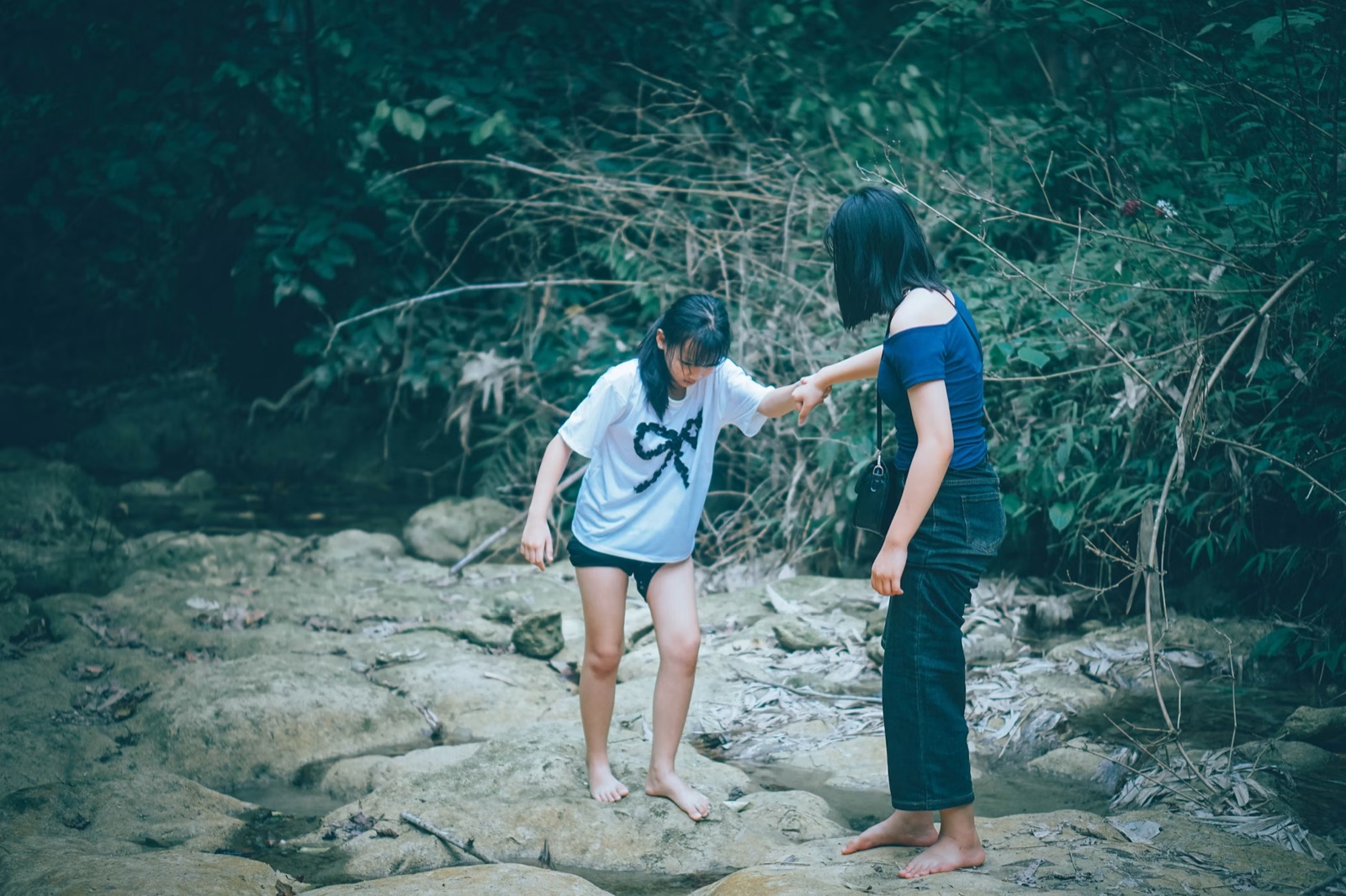 Two people helping each other across a stream, symbolizing support, momentum, and being seen through action.