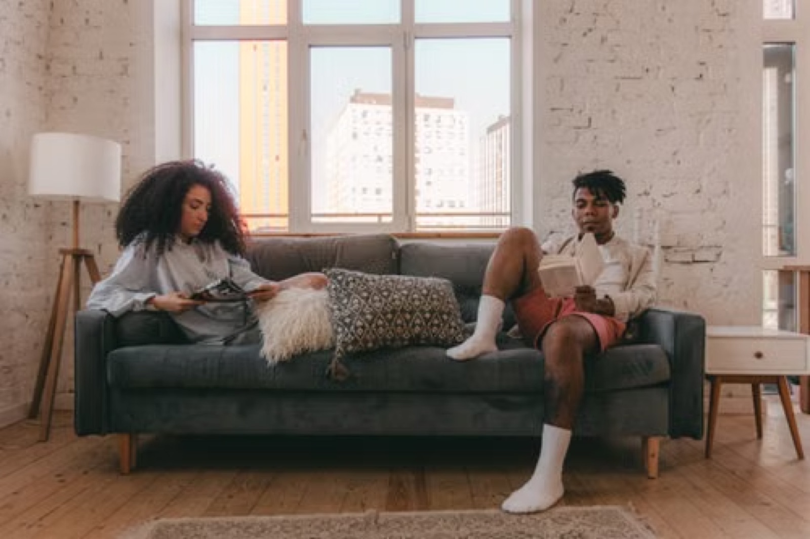 A couple sitting on the same sofa with visible distance and quiet emotional stagnation.