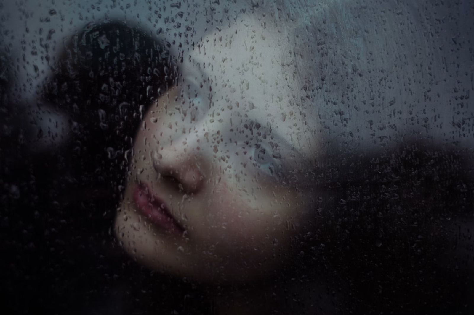 A figure seen through a rain-covered window, expressing emotional distance, sadness, and difficulty reaching through pain.