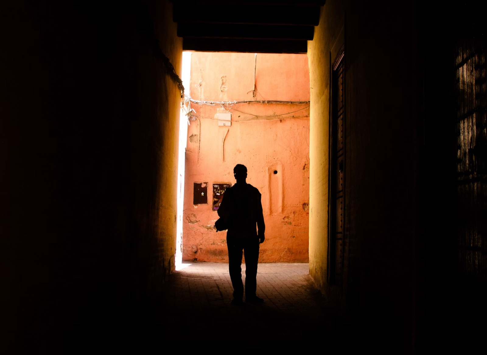 A person standing in a dim passageway with visible light ahead, echoing the feeling of being trapped but not fully without a way out.