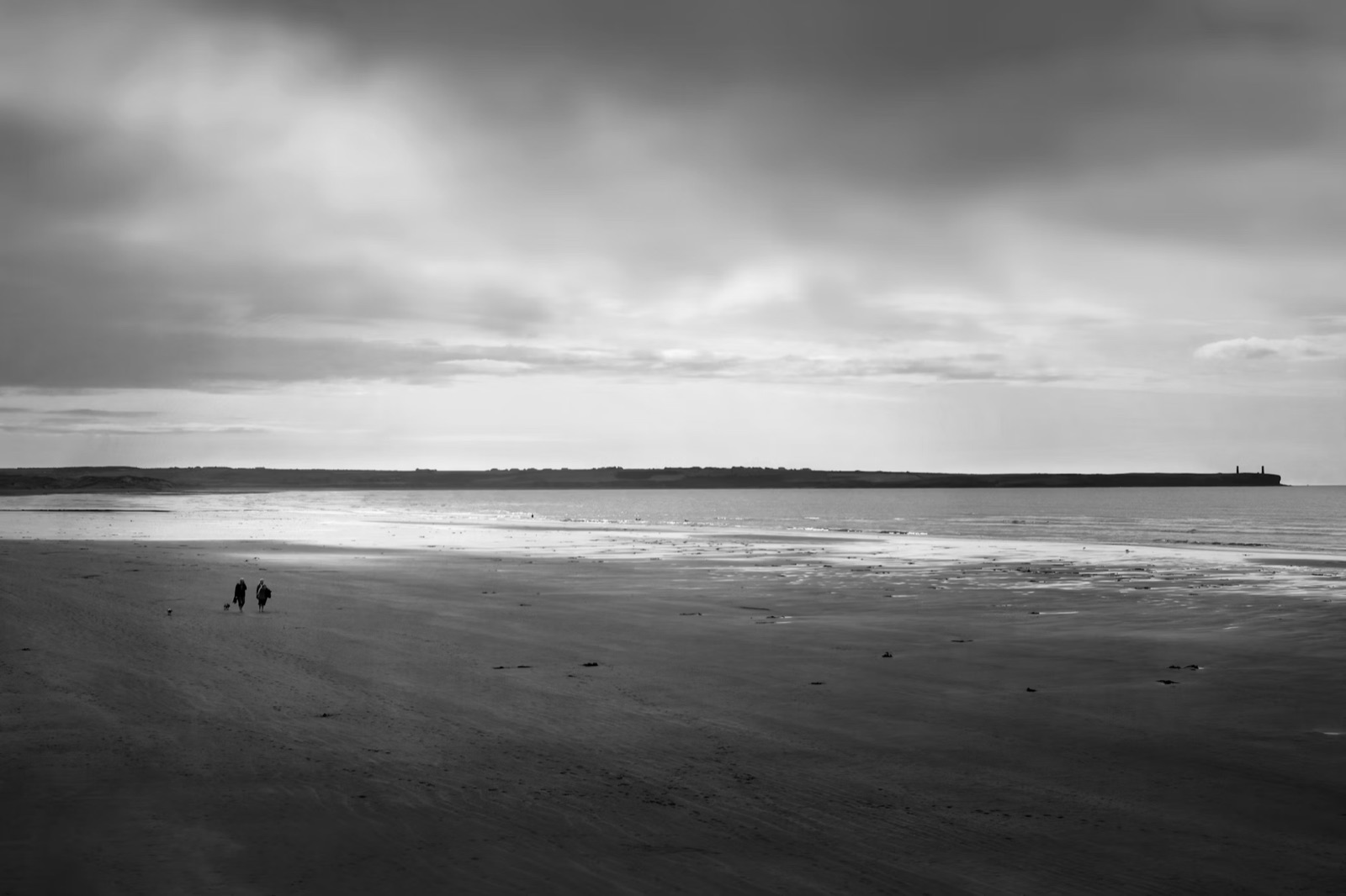 A couple walking along a beach under a cloudy sky.