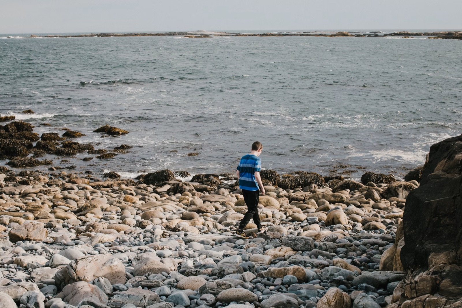 A person walking alone on a rocky beach near the ocean.