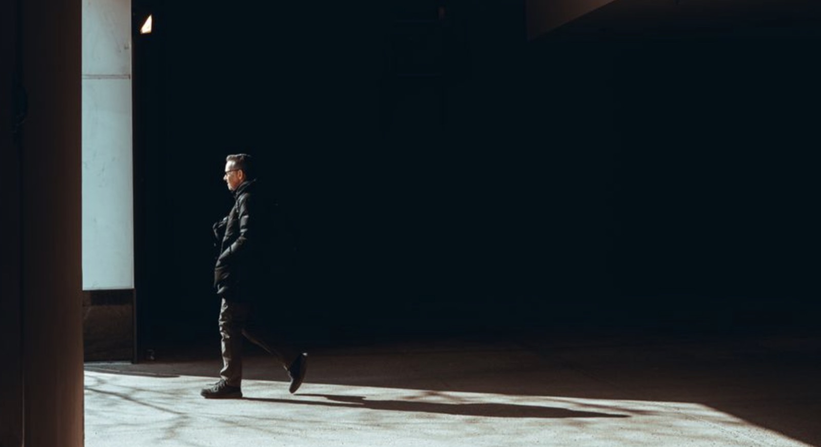 A person standing in a narrow passage toward light, representing heartbreak and the search for emotional release.