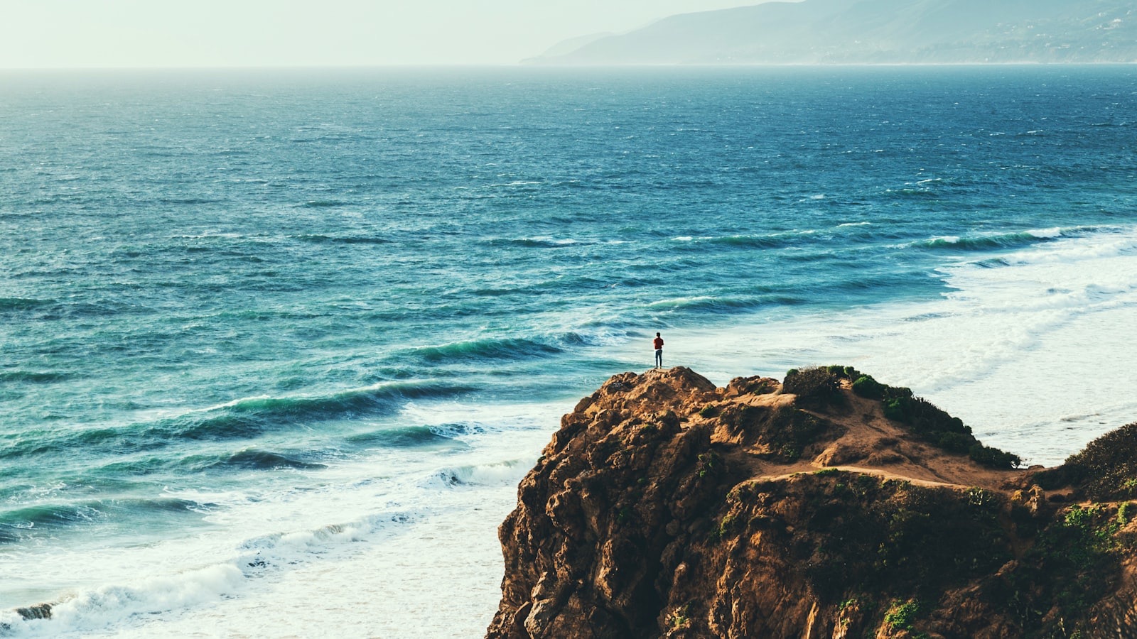 A person standing on a high point looking out over the sea, conveying an expansive view.